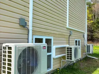Three Kerr Smart Energy ductless heat pump outdoor units on metal brackets along beige siding, with white line set covers routing the piping.