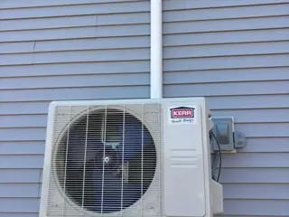 Kerr Smart Energy ductless heat pump outdoor unit on metal brackets against light blue vinyl siding, with a white line set cover running up the wall.